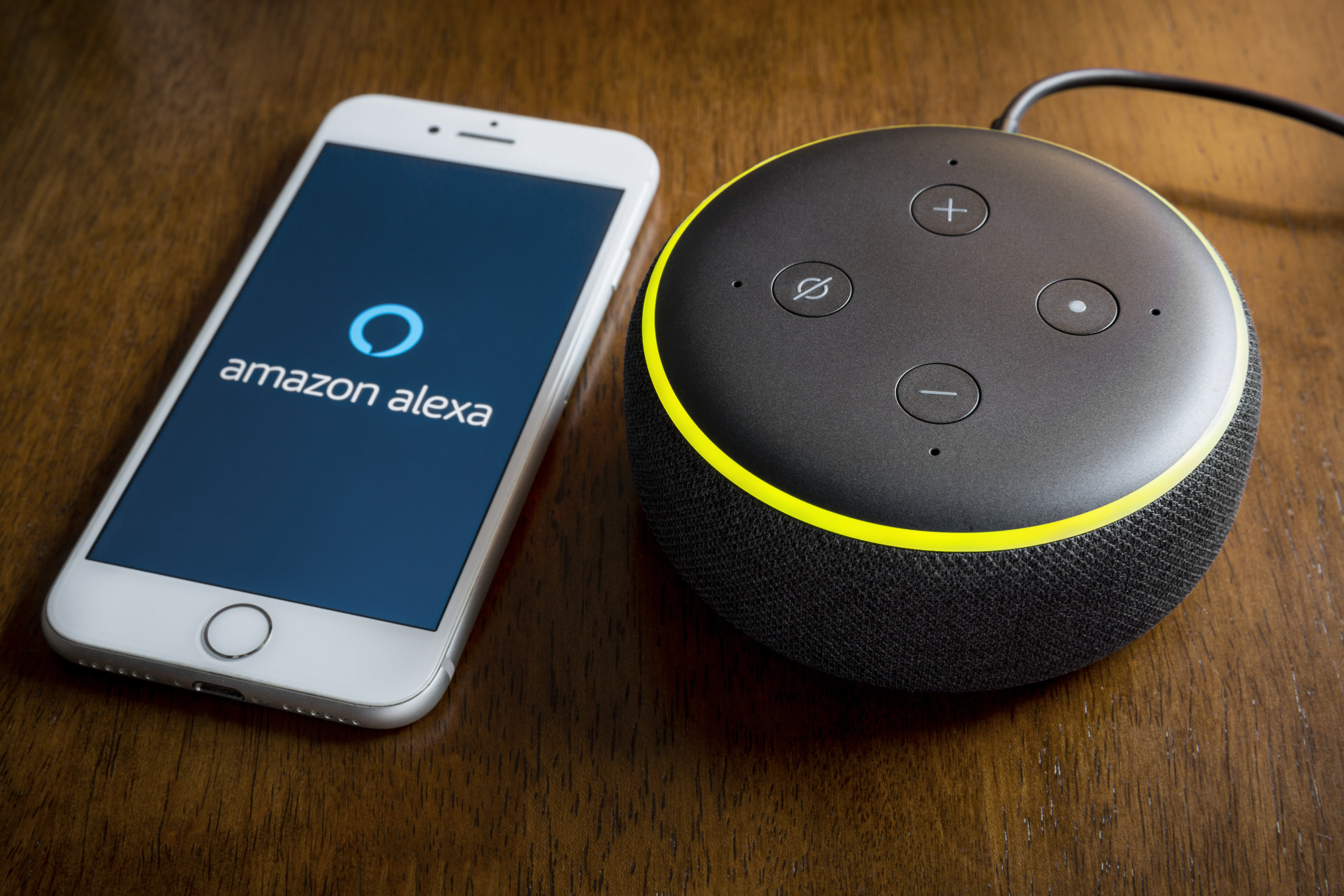 BATH, UK DECEMBER 1, 2019 : Close up of an 3rd generation Amazon Echo Dot on a desk next to an Apple iPhone running the Amazon Alexa Application